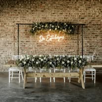 Floral-dressed bridal table beneath a neon sign in the hall